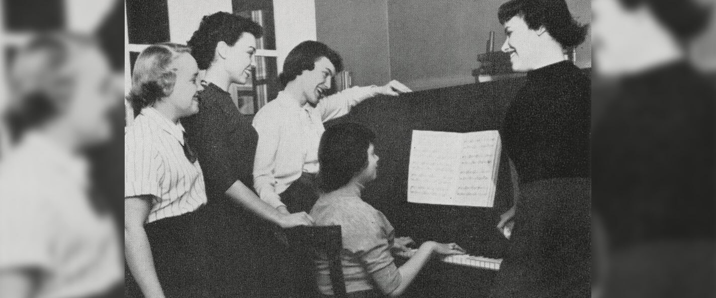 Members of Groves gathered around a piano.
