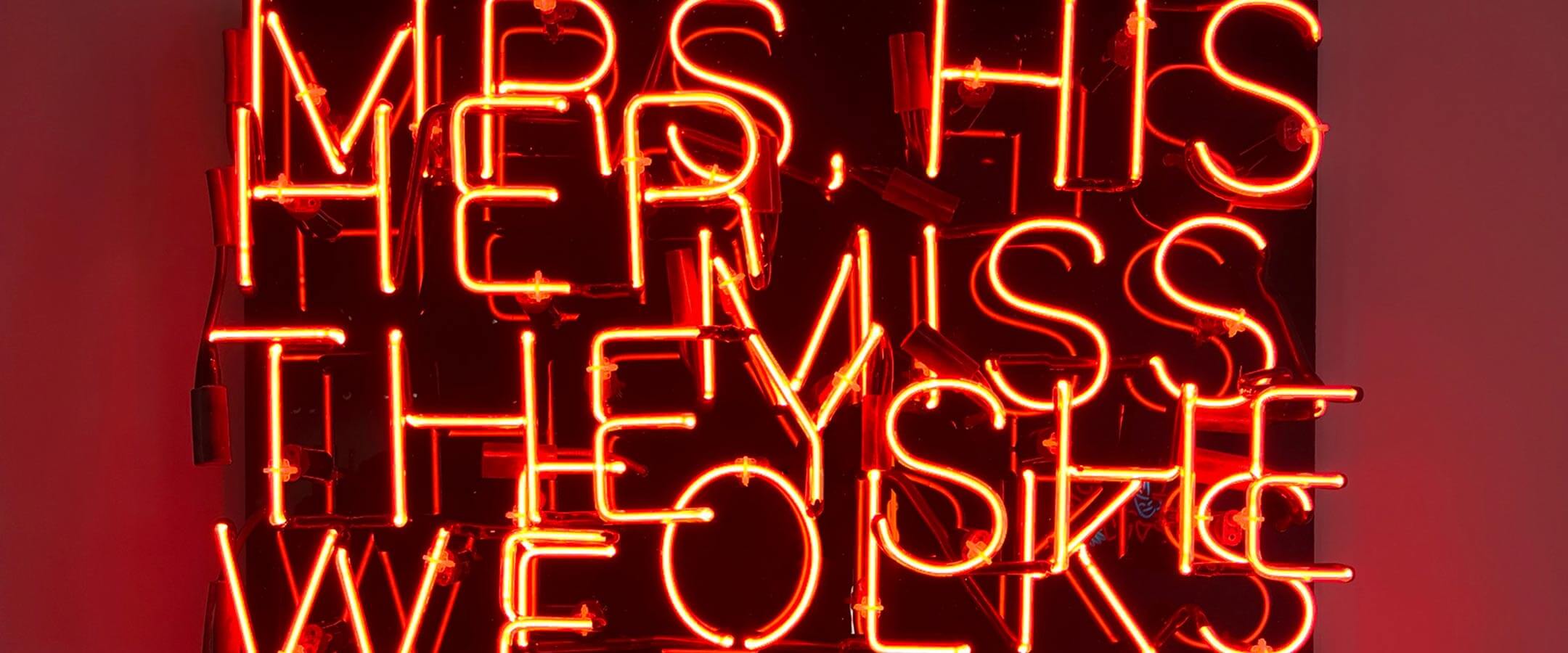 Pronouns rendered in neon red tubes are staggered on top of one another on a black background.