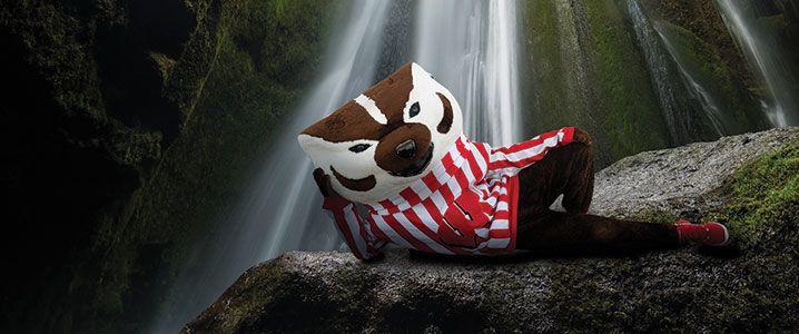 Bucky Badger lounging in cave with a waterfall in the background.